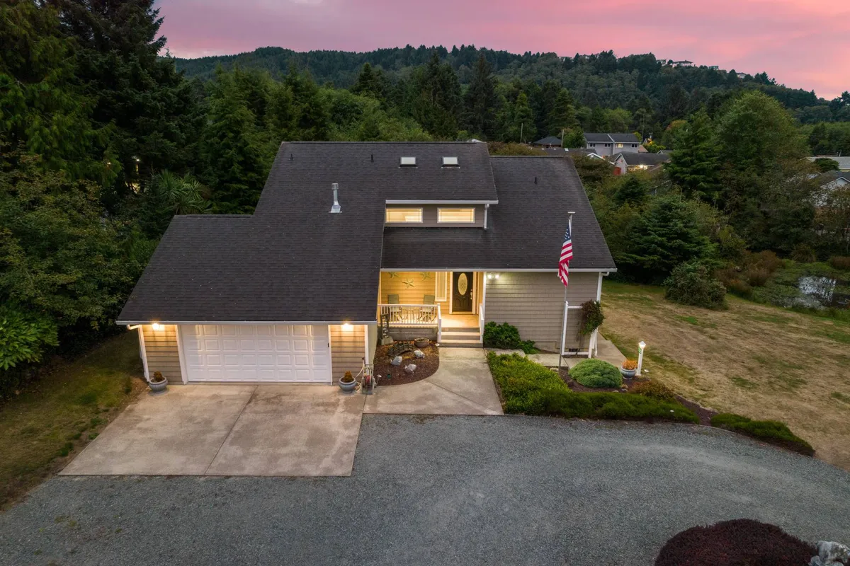The front porch of the house, adorned with an American flag and overlooking a well-kept landscaped garden and driveway, invites guests to relax and enjoy the outdoors.