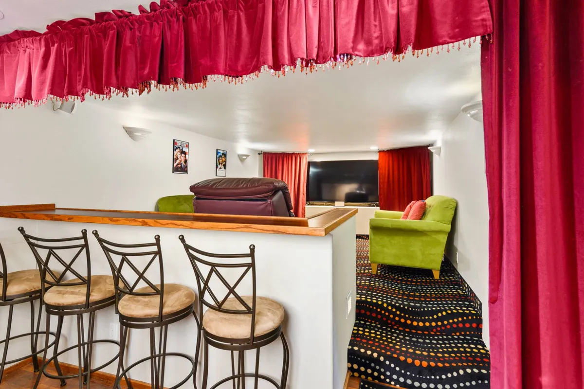A playful and cozy entertainment area featuring bar seating, a bright green couch, a large television, and red curtains. The setup is ideal for movie marathons or casual hangouts with friends, capturing the film night ambiance described in the section.