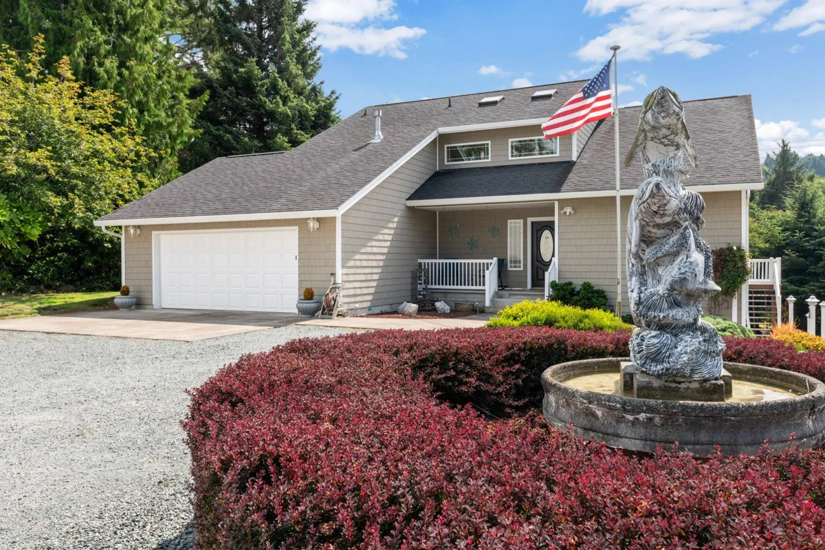 This exterior shot showcases a welcoming front porch, a landscaped yard with a fountain, and a prominent American flag. The scene radiates a sense of arrival, with outdoor spaces perfect for relaxing, greeting neighbors, or enjoying a morning coffee before exploring local attractions.