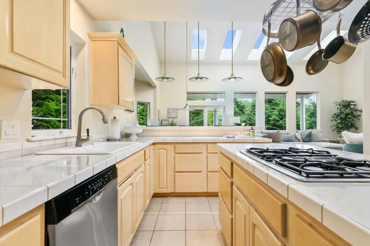 This photo highlights a modern kitchen with a prominent island, skylights above, stainless steel appliances, and a set of hanging pots and pans. The layout invites participation in meal prep and serves as a gathering hub for friends and family.