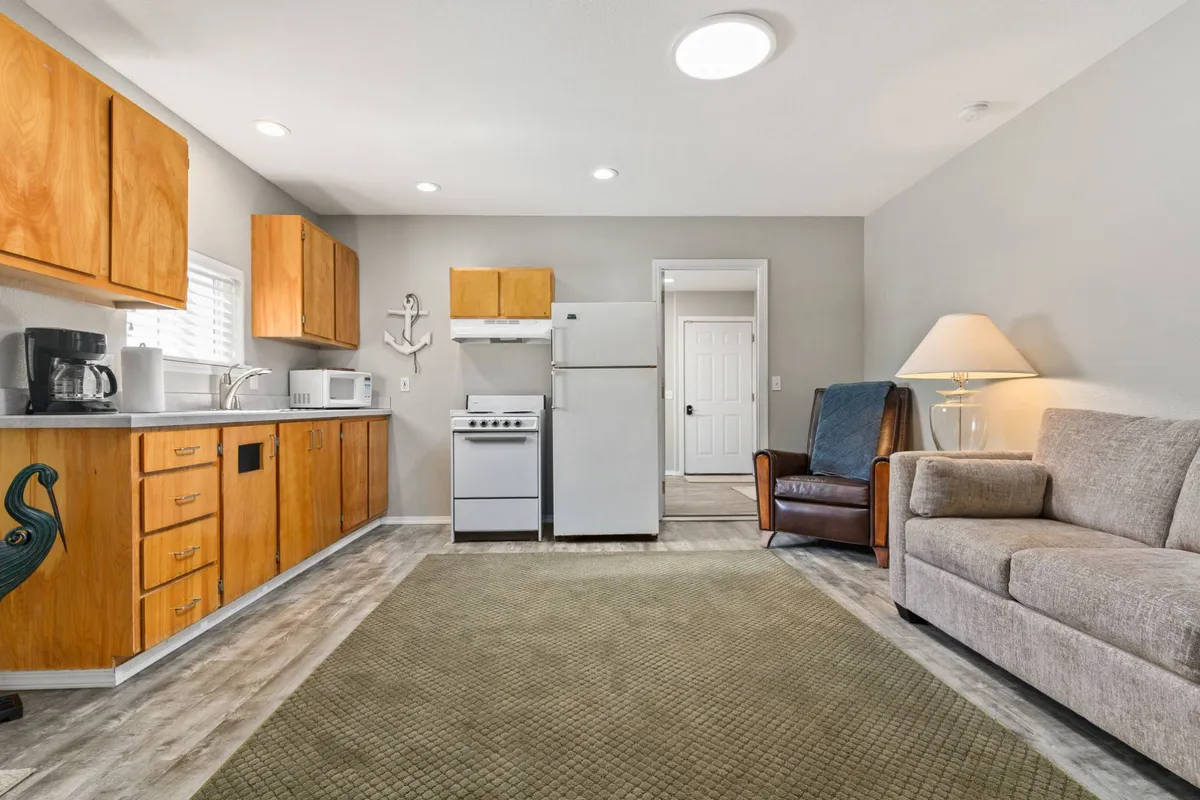 A cozy, open-plan living space in the detached apartment featuring a compact kitchen, a comfortable sofa, a dining area, and modern appliances. The arrangement encourages both privacy and togetherness, supporting extended stays or group dynamics.