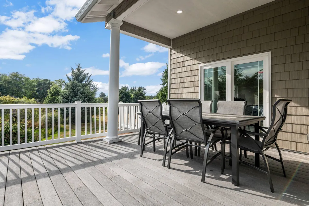 A spacious outdoor porch area with a patio table and chairs set beside a sturdy railing, overlooking a sweeping landscape view. The setting invites guests to enjoy alfresco dining, casual relaxation, or social gatherings surrounded by natural beauty.